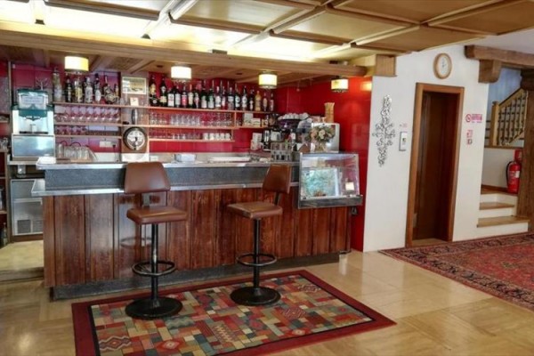 Bar s dřevěným pultem, dvěma židlemi a regálem s lahvemi a sklenicemi.