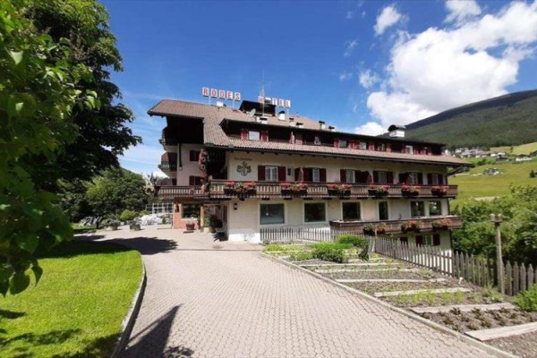 Hotel s dekorativními balkony obklopený zelení a kopci za slunečného dne.