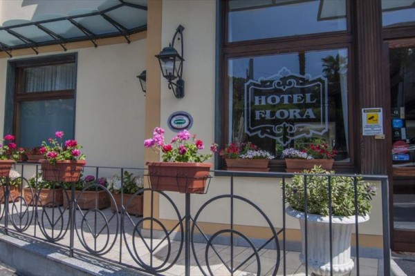 Vstup do hotelu Flora s květinami na zábradlí a okenním parapetu.