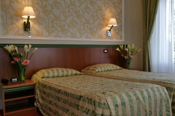 Dva jednolůžkové postele s květinami na nočních stolcích v útulném pokoji s elegantní tapetou a nástěnnými lampami.  