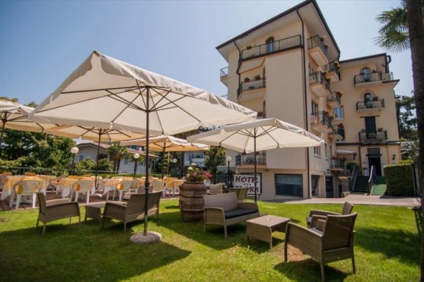 Venkovní posezení s ratanovým nábytkem a slunečníky před budovou hotelu.