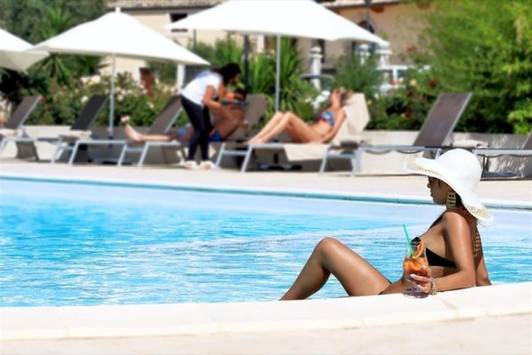 Žena s kloboukem relaxuje v bazénu s koktejlem v ruce.