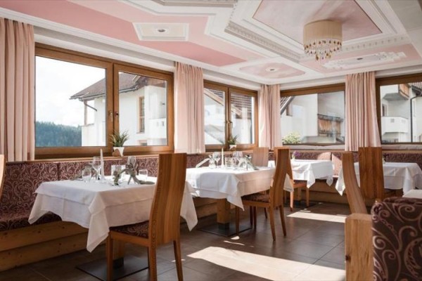 Restaurace s růžovými závěsy a prostřenými stoly u okna.