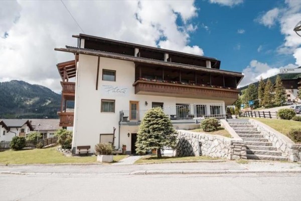 Třípatrová budova hotelu obklopená zelení s modrou oblohou.