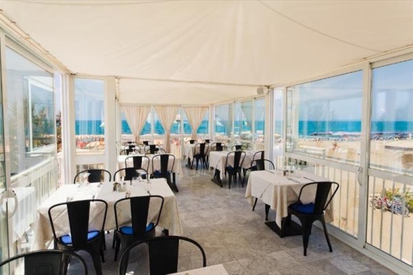 Restaurace s výhledem na pláž a moře za prosklenými stěnami.