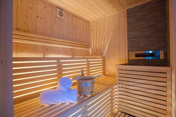 Dřevěná sauna s lavicemi, ručníkem a vědrem s naběračkou.