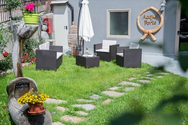 Zahradní posezení s ratanovými křesly a slunečníkem na trávníku před šedou budovou s nápisem 