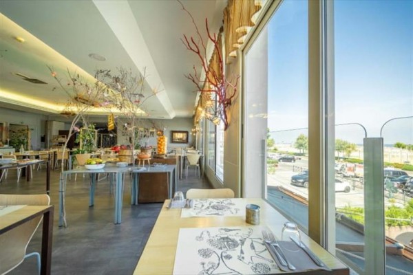Moderní restaurace s velkými okny a dekorativními větvemi u stolů.