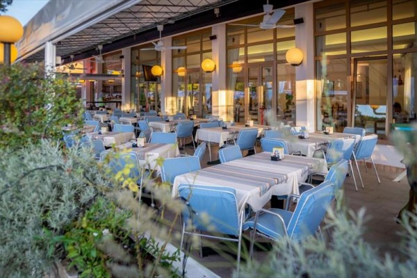 Venkovní terasa restaurace s modrými židlemi a prostřenými stoly pod přístřeškem.