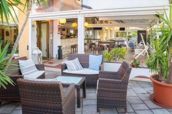 Venkovní terasa s ratanovým nábytkem a polštáři před otevřenou restaurací.