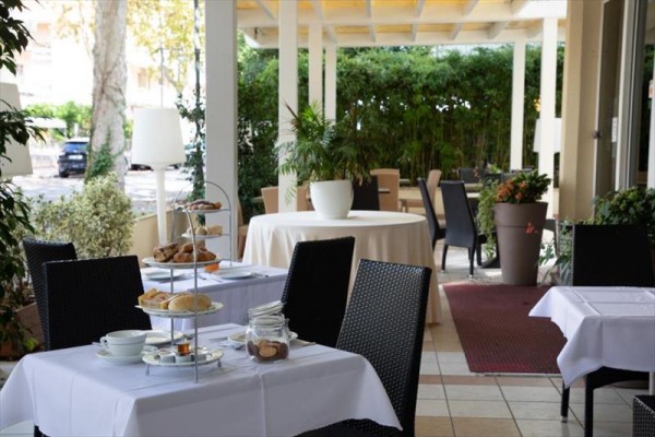 Zahradní restaurace s prostřenými stoly a rostlinami kolem.