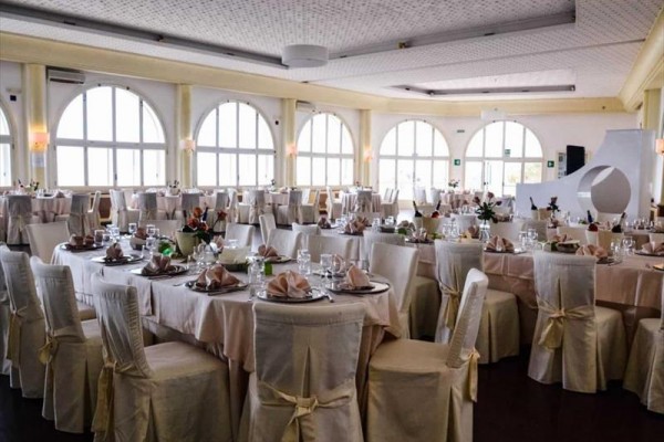 Elegantně prostřená jídelní hala s kulatými stoly a bílými potahy na židlích.