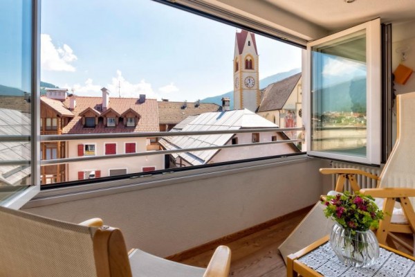 Balkon s výhledem na střechy domů a kostelní věž.