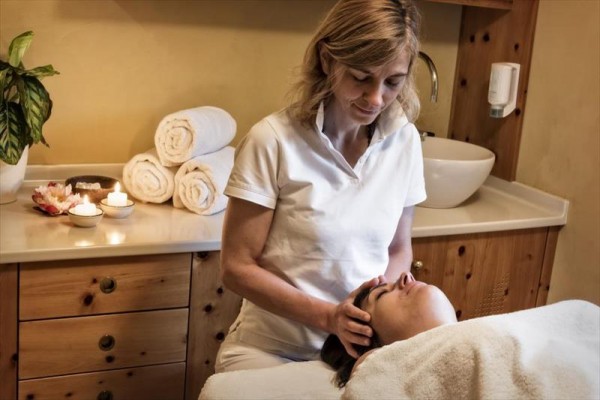 Masérka provádí masáž hlavy v relaxační místnosti s dekoračními svícemi.