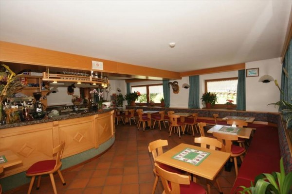 Restaurace s dřevěným nábytkem, barem a květinami na oknech.