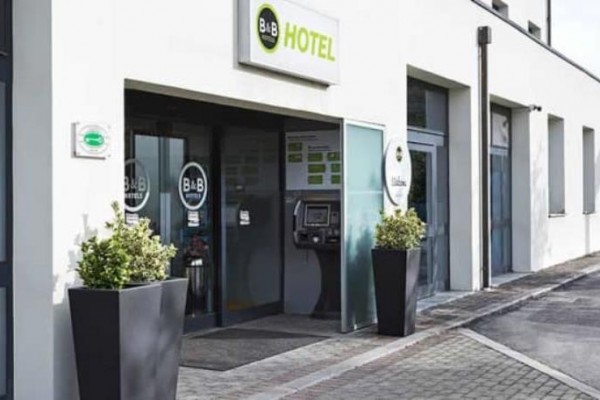 Vstup do moderního hotelu s automatickým recepčním terminálem a květináči.