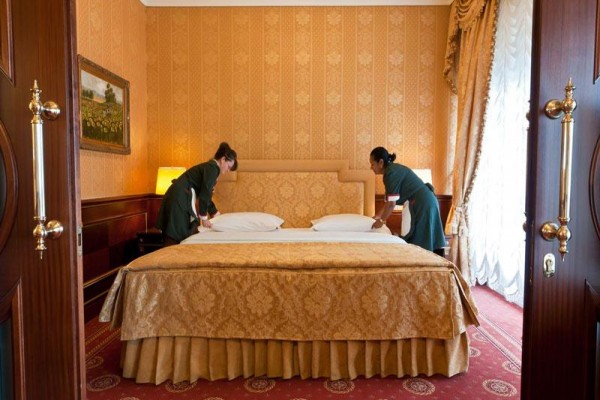 Dvě pokojské ustelují manželskou postel v luxusním hotelovém pokoji.  