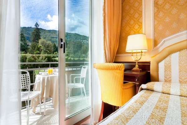 Elegantní hotelový pokoj s výhledem na balkon a hory v pozadí.