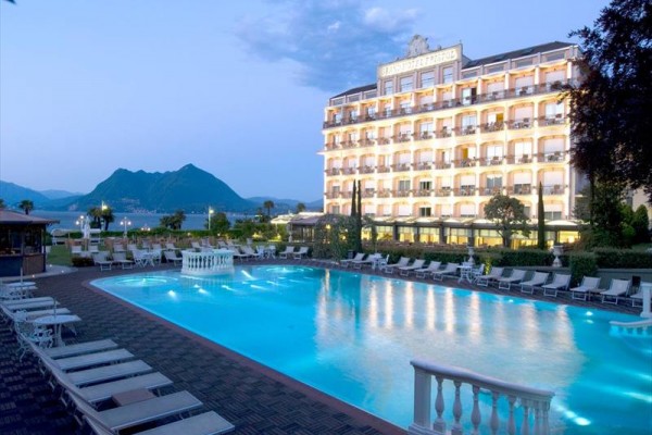 Osvětlený hotel u venkovního bazénu s horami v pozadí.