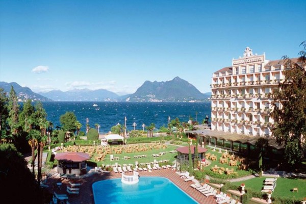 Hotel u jezera s bazénem a horami v pozadí.