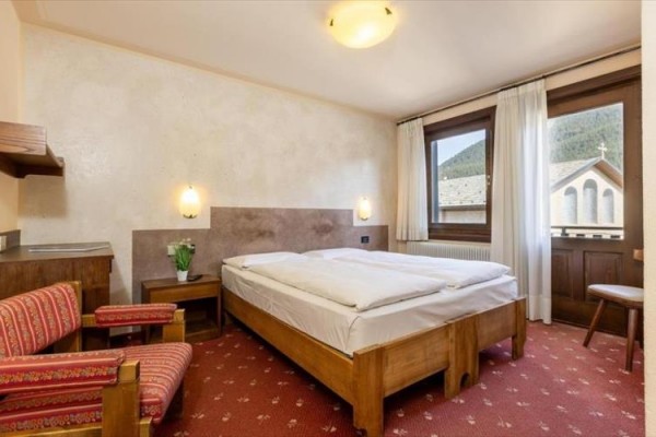 Hotelový pokoj s manželskou postelí, dvěma křesly a výhledem na kostel.