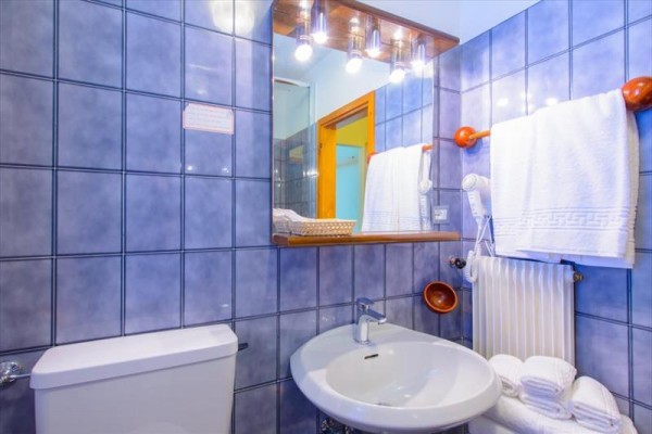 Koupelna s modrými dlaždicemi, umyvadlem, zrcadlem a ručníky na topení.