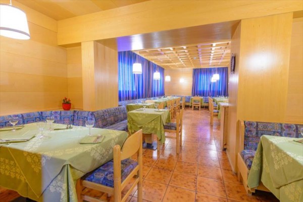 Restaurace s dřevěným interiérem, modrými závěsy a zelenými ubrusy.