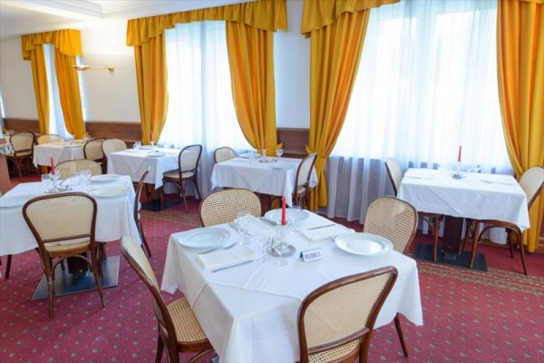 Restaurace s kulatými stoly, židlemi a žlutými závěsy.
