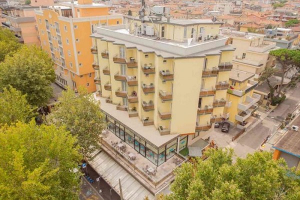 Výšková budova s balkony a terasou uprostřed městské zástavby.