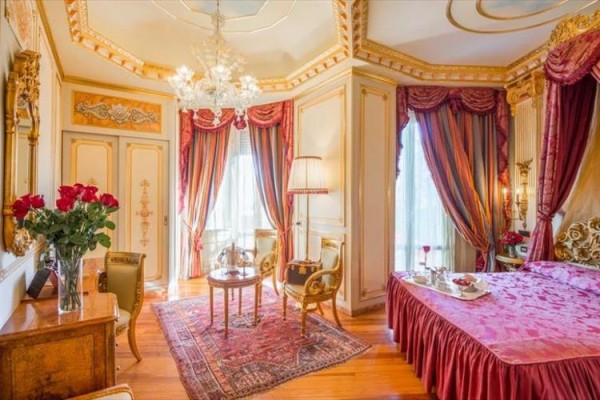 Luxusní pokoj s elegantním nábytkem, zlatými detaily a červenými závěsy.  