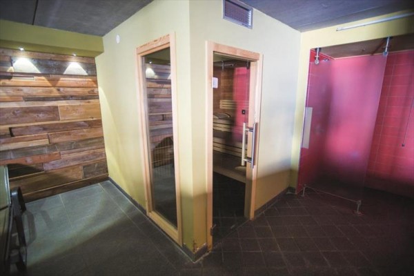 Sauna s dřevěným obložením a skleněnými dveřmi vedle sprchy.