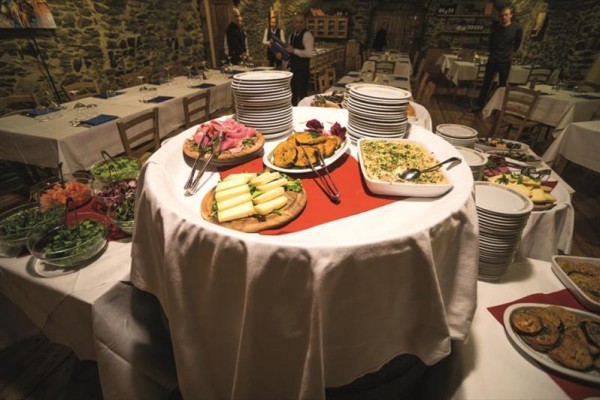 Kulatý stůl plný různých druhů předkrmů a talířů v rustikální restauraci.