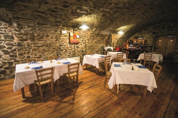 Restaurace s kamennými zdmi a dřevěnou podlahou, stoly s bílými ubrusy.