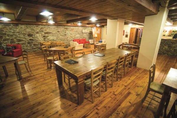 Dřevěný interiér restaurace s kamennými zdmi a židlemi rozmístěnými kolem stolů.  