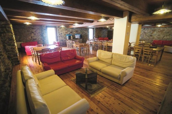 Prostorný interiér s dřevěnou podlahou, kamennými zdmi, křesly a stoly.