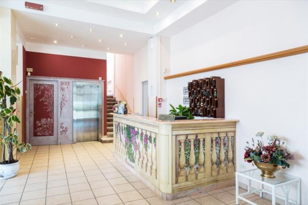 Recepce hotelu s dekorativně vyzdobeným pultem a výtahem v pozadí.