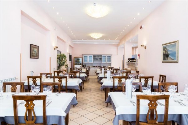Elegantní restaurace s bílými a šedými ubrusy na stolech a dřevěnými židlemi.
