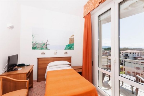 Jednolůžkový pokoj s oranžovým povlečením, televizí na stole a výhledem na balkon skrz skleněné dveře.
