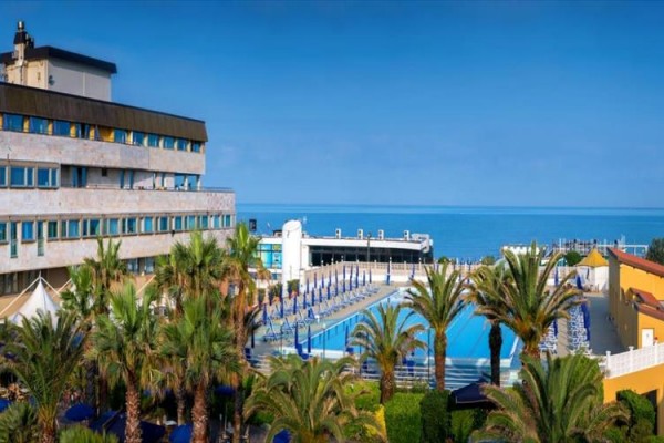 Hotel s bazénem obklopený palmami u moře.