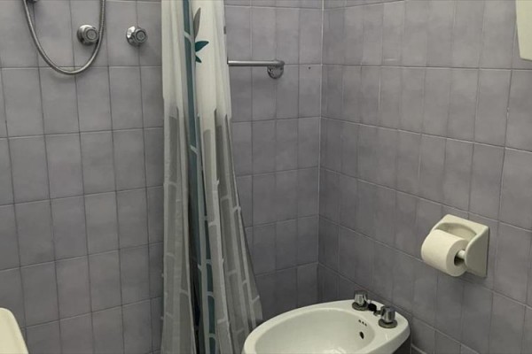 Koupelna s šedými obklady, sprchovým koutem, umyvadlem, bidetem a toaletním papírem na stěně.
