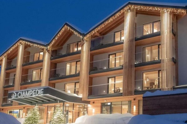 Moderní dřevěný horský hotel v zimě s osvětlením a sněhem na střeše.
