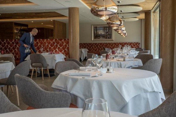 Elegatní restaurace s kulatými stoly a číšníkem připravujícím stůl.
