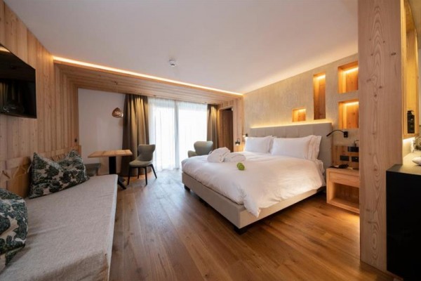 Moderní hotelový pokoj s manželskou postelí, dřevěným interiérem a velkým oknem na balkon.
