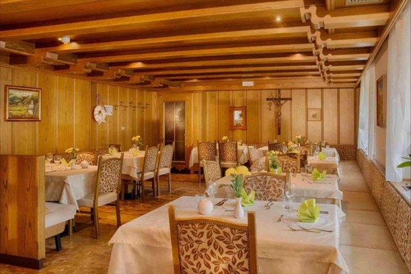 Restaurace s dřevěným obložením, stoly pokryté bílými ubrusy a zelenými ubrousky.