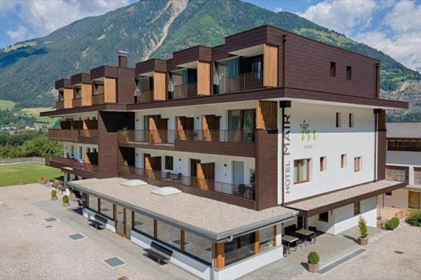 Moderní hotel s dřevěnými balkony před horským panoramatem.