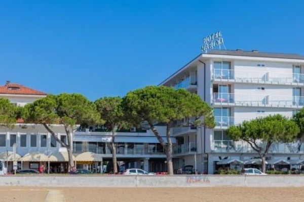 Moderní hotel s balkony a zelenými stromy v popředí.