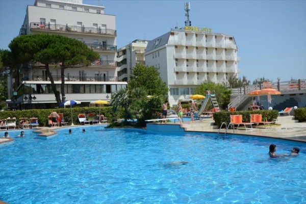 Venku je bazén s lidmi a v pozadí několikapatrový hotel.