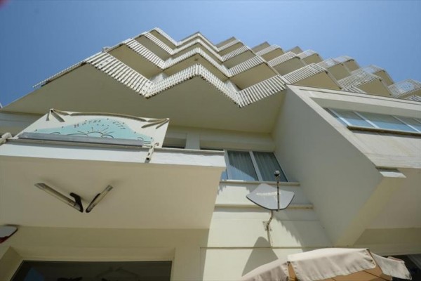 Pohled vzhůru na balkóny moderní budovy s modrou oblohou v pozadí.