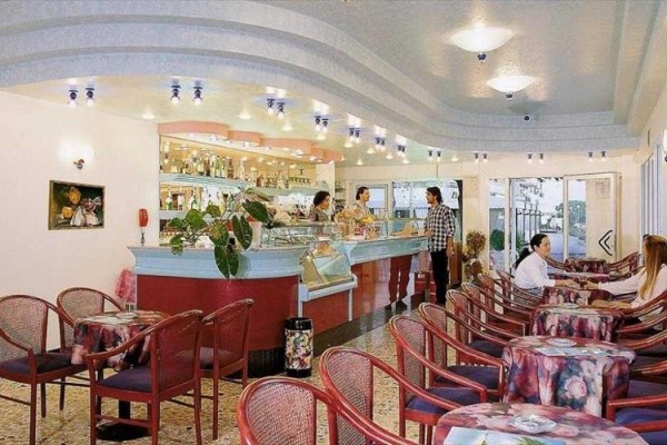 Restaurace s obloukovým barem, stoly a lidmi posedávajícími uvnitř.