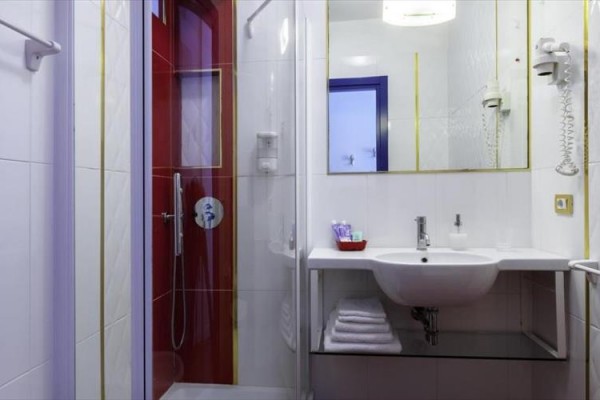 Moderní koupelna s bílým umyvadlem a sprchovým koutem s červenými dveřmi.